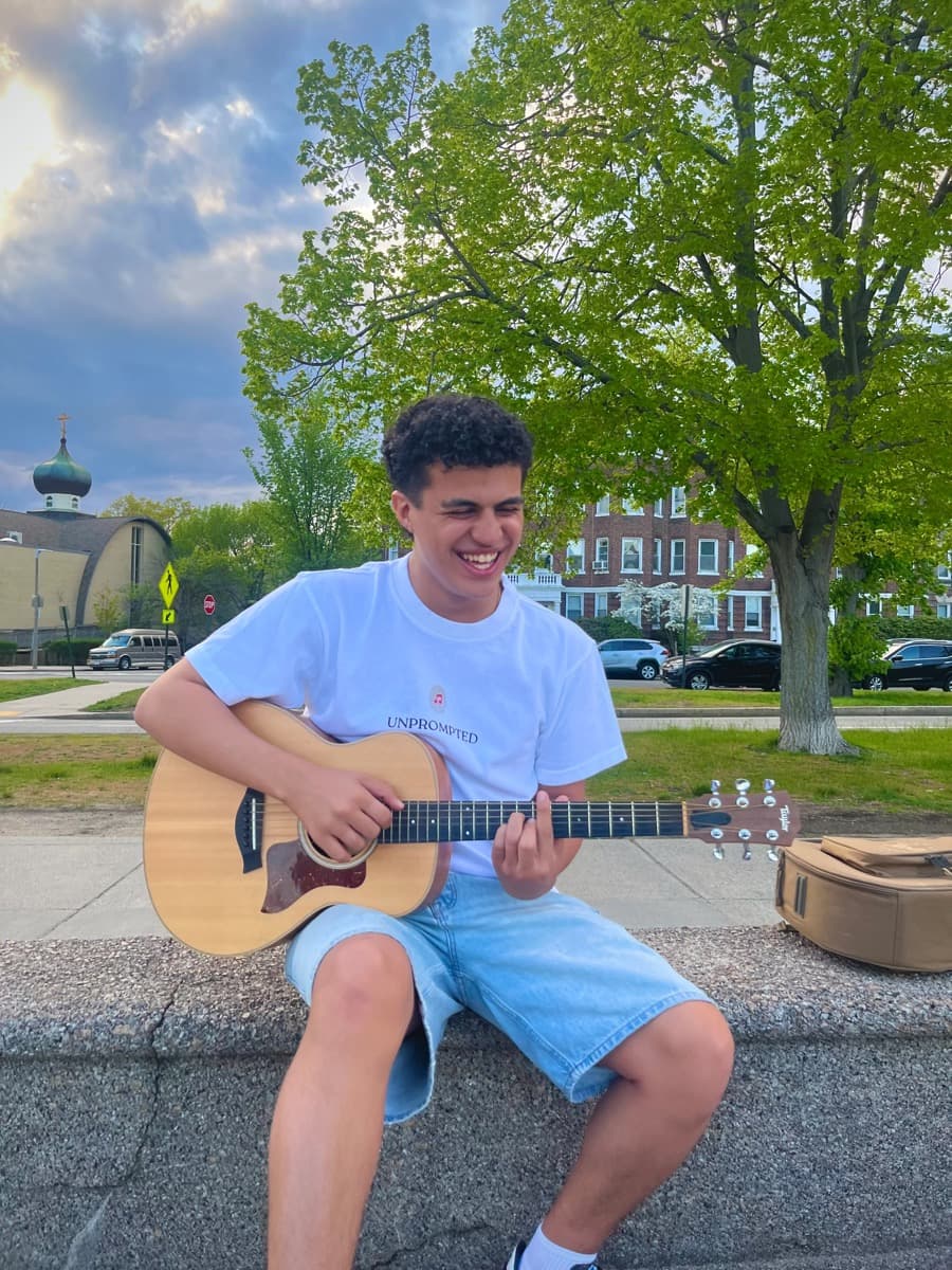 A musician smiling while playing guitar outdoors